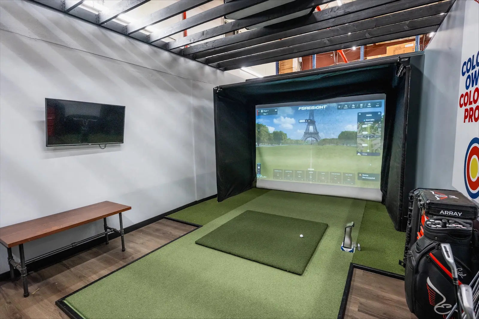 Indoor golf simulator setup with The SportScreen enclosure displaying a golf course, bench, and golf bag.