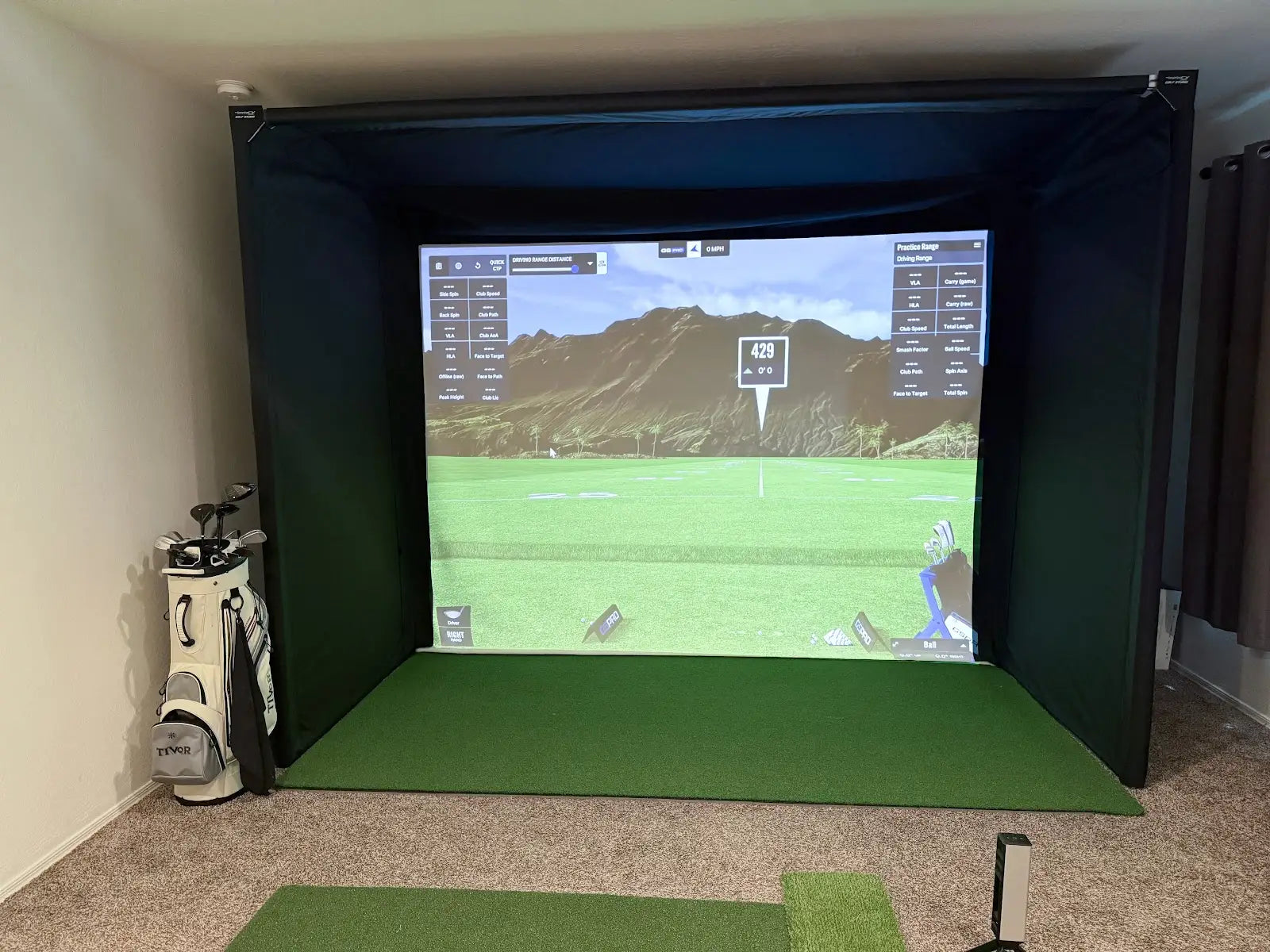 Indoor golf simulator setup with The SportScreen enclosure displaying a golf course, golf clubs, and mat.