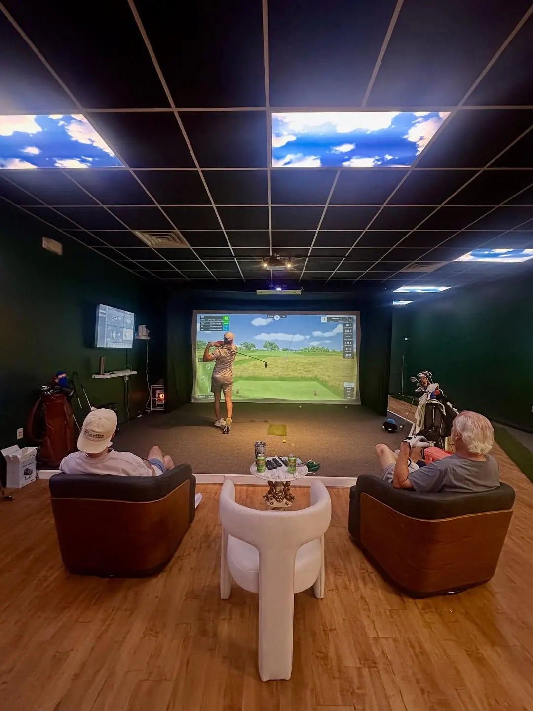 Indoor golf simulator setup with The SportScreen enclosure and two people playing on a screen.