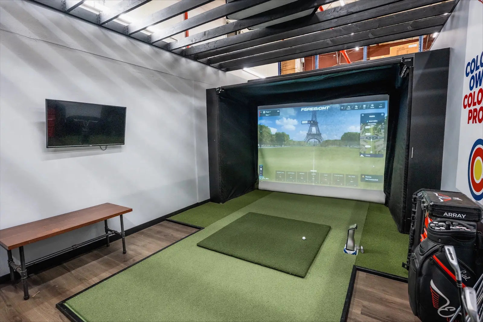 Indoor golf simulator setup with The SportScreen enclosure displaying a golf course and bench on the side.