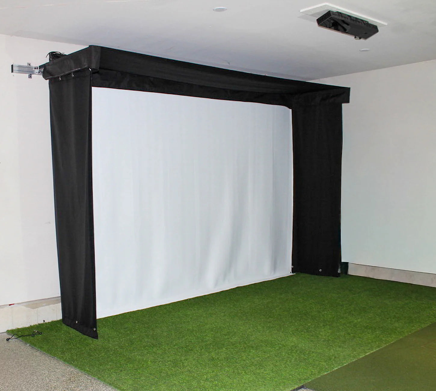 Indoor golf simulator setup with green turf and white screen. SportScreen Vanish Lite Retractable enclosure.