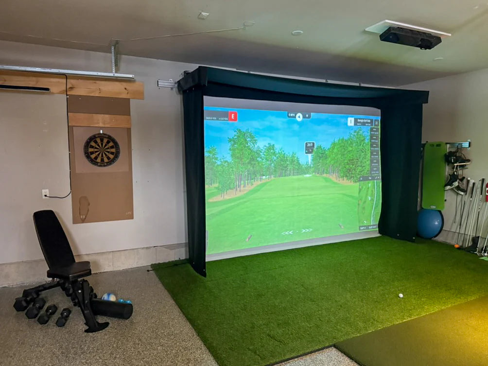 Indoor golf simulator setup with screen displaying a golf course, chair, and various equipment. SportScreen Vanish Lite Retractable Golf Simulator enclosure.