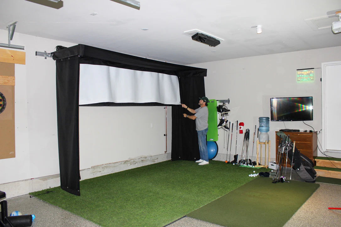 Indoor golf simulator setup in a home garage with a person using it. SportScreen Vanish Lite Retractable Golf Simulator enclosure.