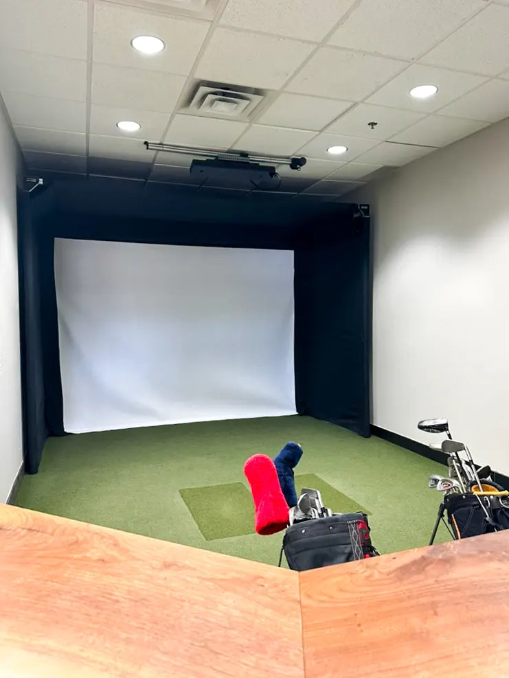 Golf simulator setup with SportScreen enclosure, chairs, and equipment in a room.